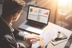 Image of man looking at graphs on a paper and computer screen