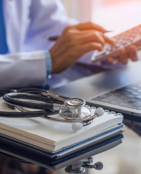 Image of Person typing on a calculator with papers, a laptop and a stethoscope in front of them