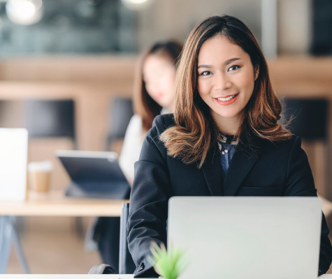 Image of Asian woman at a laptop, smiling at the camera