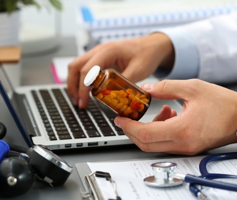 Image of doctor holding a prescription bottle while typing on a computer